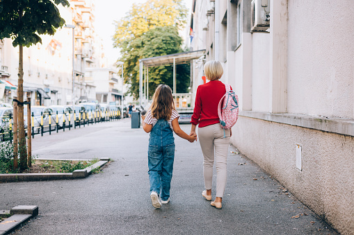 Senior woman walking her granddaughter to school, holding her hand, first day of school concept.