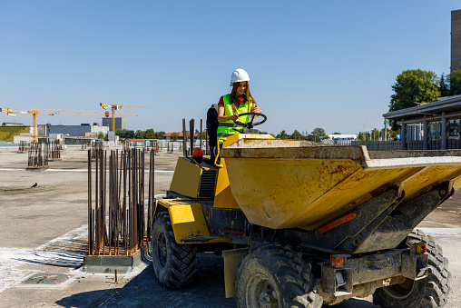 A Young Female Construction Worker is Driving a Dump Truck at the Construction Site.