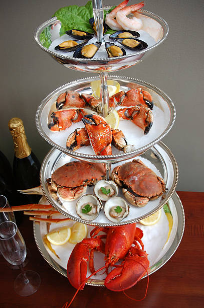 Seafood Tower An impressive display of chilled fresh seafood on a multilayered silver tower, including cocktail shrimp, mussels, Jonah crab claws, whole crabs, clams on the half shell, snow crab legs, and lobster.  snow crab photos stock pictures, royalty-free photos & images