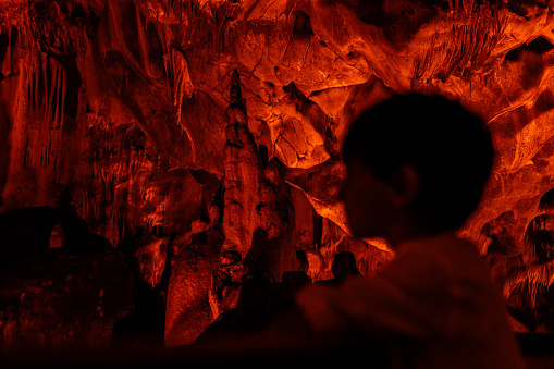 The boy wanders around the cave and explores. Natural formations are visible in the illuminated cave. Abstract shapes were formed with the effects of shadow and light. Shot with a full frame camera.