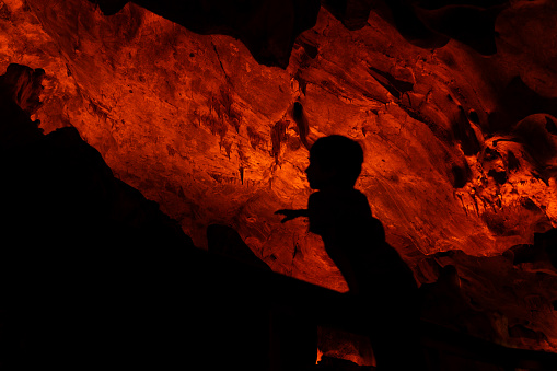 The boy wanders around the cave and explores. Natural formations are visible in the illuminated cave. Abstract shapes were formed with the effects of shadow and light. Shot with a full frame camera.