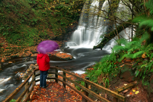 Hiking woman watching the Ess-na Crub Waterfall on a rainy day in the Glenariff forest park, County Antrim, Northern Ireland. Long exposure - there are some blurred spots due to raindrops & slow shuttertime.