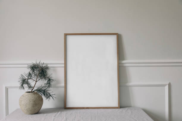 istock Minimal Christmas Scandinavian interior. Winter art display. Front view of blank vertical wooden picture frame, poster mockup. Pine tree branches in old vase on table. Elegant white wall background 1701117436