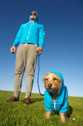 Man stands with dog each in matching blue hooded sweatshirts on bright green grass