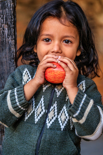 Happy little Nepali girl eating an apple, she lives in Bhaktapur. Bhaktapur is an ancient town in the Kathmandu Valley and is listed as a World Heritage Site by UNESCO for its rich culture, temples, and wood, metal and stone artwork.