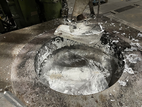 a ladle in an aluminum melting furnace in an installation of an aluminum die casting injector, in the furnace the molten material and solidified alumina splashes around, horizontal