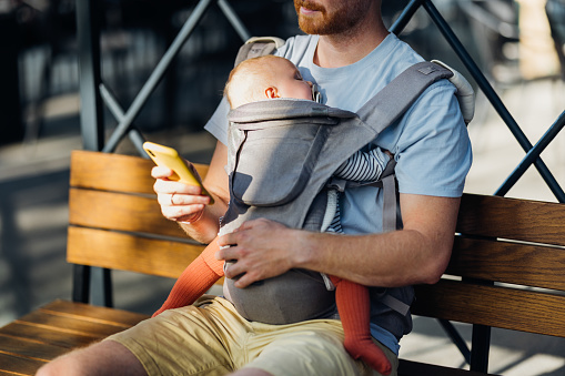 An urban dad embraces the joys of parenthood, carrying his daughter close in a baby carrier while exploring the city.