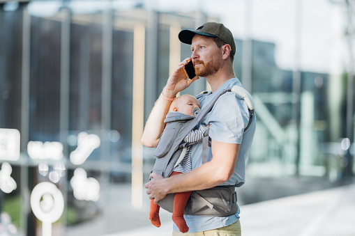 An urban dad embraces the joys of parenthood, carrying his daughter close in a baby carrier while exploring the city.
