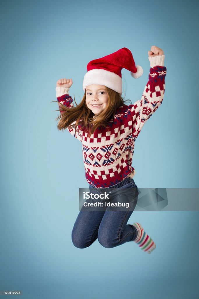 Santa's Happy Little Helper Jumping for Joy Color image of an excited little girl leaping into the air . She is wearing a Santa hat and an ugly Christmas sweater. Christmas Stock Photo