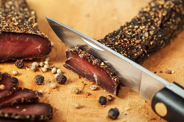 Biltong - traditional South Africa delicacy; raw beef with spices and salt dried on air; pocket knife with chunks of meat and spices;