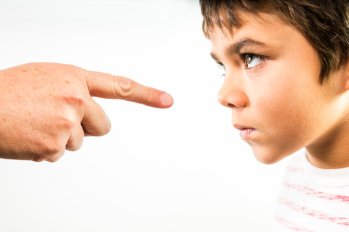 A photograph of a little boy being disciplined.  An angry child stares back in anger and defiance as he is being disciplined.  The finger of an adult is pointing directly at him.  