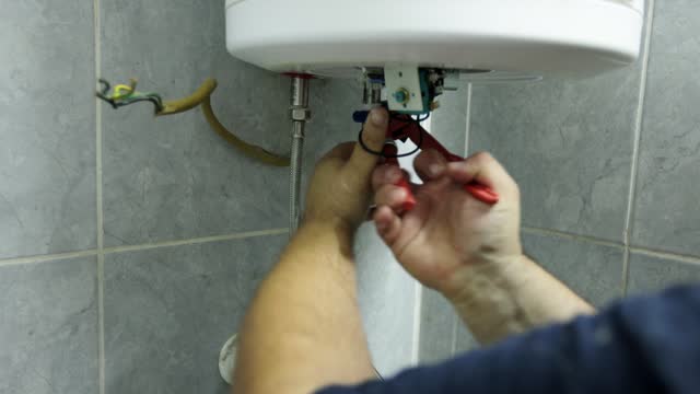 Caucasian male heating engineer using pliers to repair a boiler at the customer domestic bathroom
