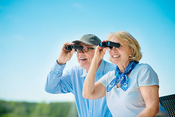 Active Senior Couple Senior Couple looking though binoculars outdoors. couple hope sky blue stock pictures, royalty-free photos & images
