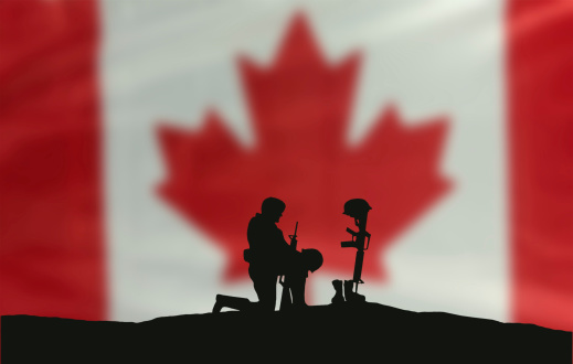 A soldier kneeling in front of the grave of a fallen soldier. A Canadian flag in the background.