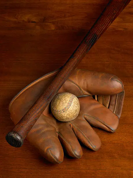 An antique baseball glove,bat and baseball on a wood background. Warmly lit for a nostalgic feeling. 