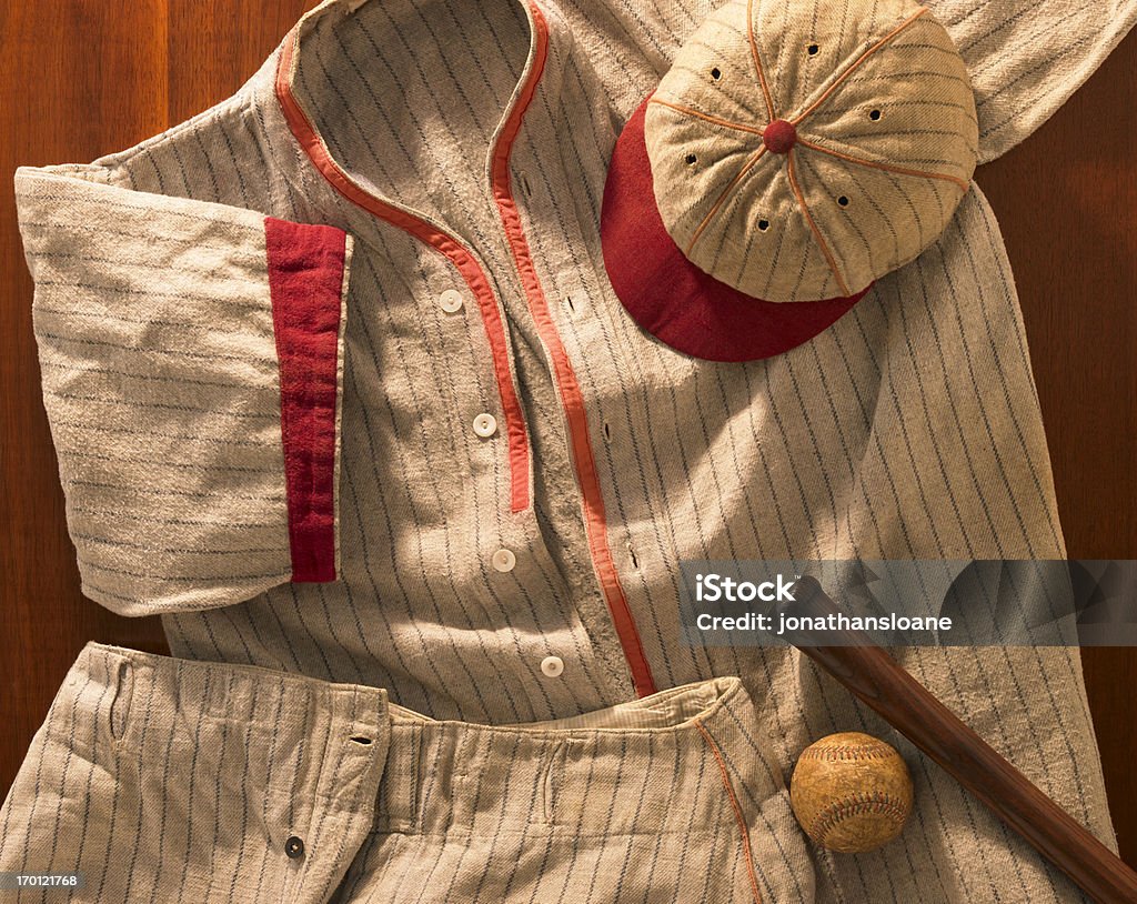 Old-time wool baseball uniform with cap, pants and bat A shot of an antique pin-striped wool baseball uniform from the 20's with a matching cap and pants. Warm dramatic lighting used to emphasize the nostalgic mood. This is the real thing! Baseball - Ball Stock Photo