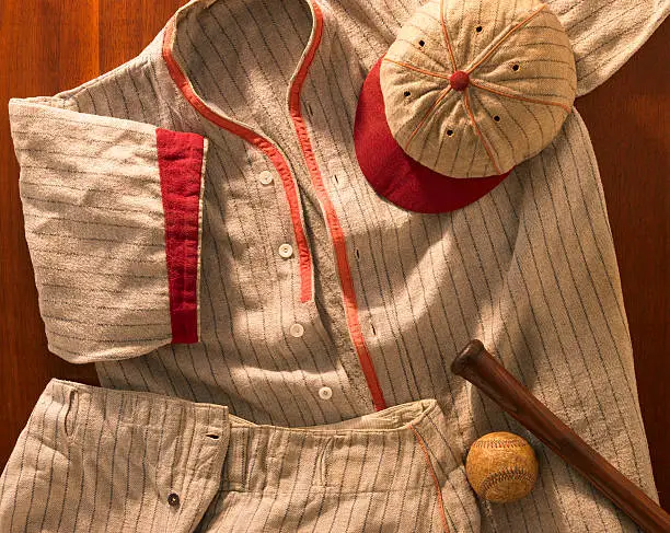 A shot of an antique pin-striped wool baseball uniform from the 20's with a matching cap and pants. Warm dramatic lighting used to emphasize the nostalgic mood. This is the real thing!