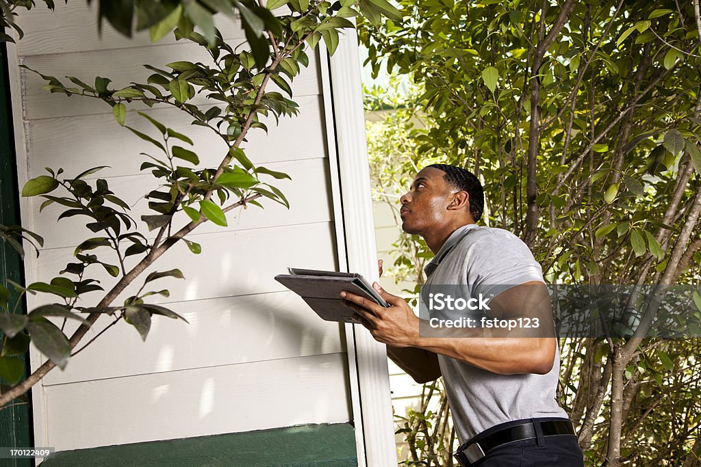 Home inspection on exterior.  Using digital tablet to record results Home inspection checking exterior of home being sold.  Inspector is using digital tablet to record results. Examining Stock Photo