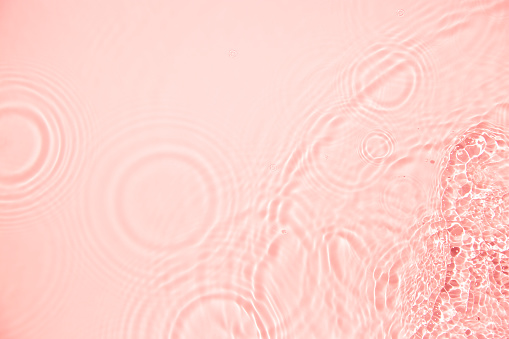 Close-up, directly above on clean transparent coral colored water waves and drops with copy space.