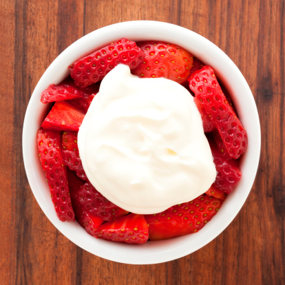 Top view of white bowl full of strawberries with whipped cream