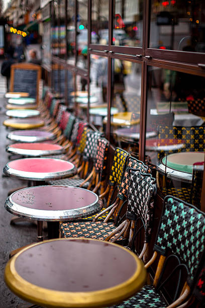 Row of Outdoor Parisian Cafe Tables A row of sidewalk tables set against the glass wall of a Parisian cafe. Tables are wet due to recent rain. Shallow focus shot, focus is on cafe table. rainy cafe stock pictures, royalty-free photos & images