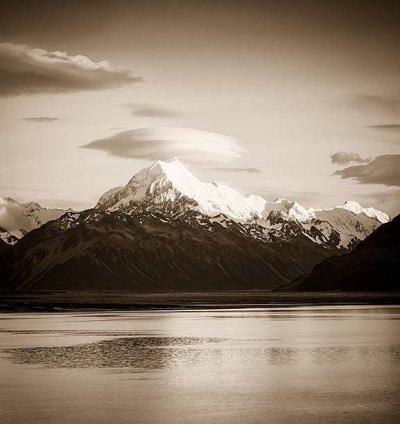 Toned monochrome image of early morning sunlight illuminating the snow and ice on the peak of Mt Cook (Aoraki), topped by a lenticular cloud, on New Zealand's South Island.