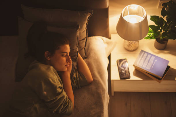 lampe éclairant une jeune femme endormie. - lampe de chevet eclairage femme photos et images de collection