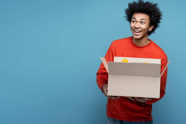istock Young attractive overjoyed African American man influencer unpacking box 1701339524