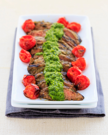 Sliced hanger steak with roasted tomatoes and chimichurri sauce.