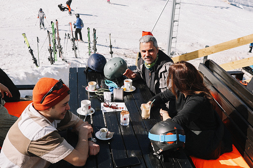 People having a break from skiing in the Alps, drinking and having fun at the outdoors cafe near the ski slope.