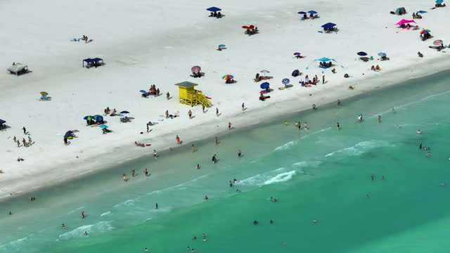View from above of Siesta Key beach with white sands full of tourists in Sarasota, USA. Many people enjoing vacation time swimming in Mexica gulf water and relaxing on warm Florida sun