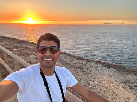 Tourist takes selfie at sunset on the beach in Potugal carrying camera around neck