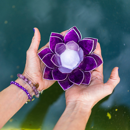 Top angle view of hands holding a purple glass lotus over water. Yoga and meditation concept.