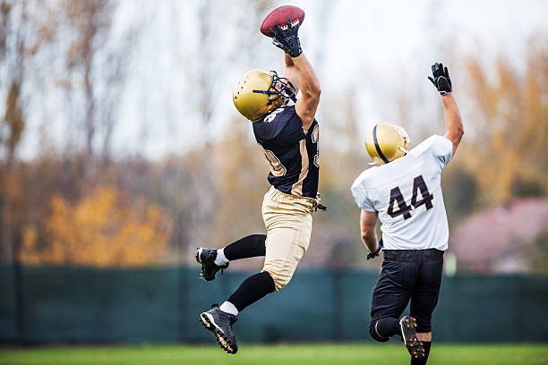 American football player catching a ball. Two American football players in action.   wide receiver athlete stock pictures, royalty-free photos & images
