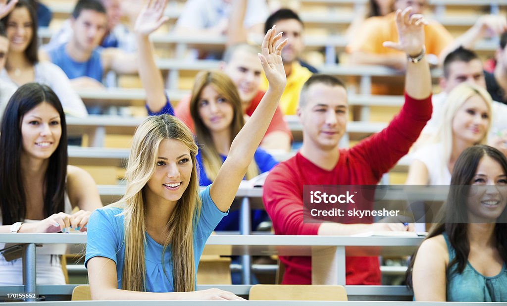 Estudiantes en el aula de conferencias con aumento de las manos. - Foto de stock de Alzar la mano libre de derechos