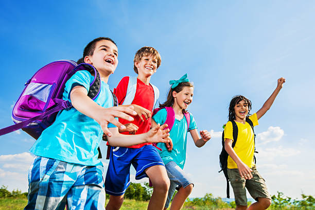 Two little boys wearing blue backpacks or schoolbags running to school on a narrow dirt path between fences. Beautiful autumn sepetmber day.