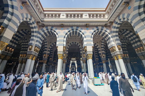 Medina, Saudi Arabia - March 09, 2023: Muslim pilgrims walk in the courtyard of Masjid al-Nabawi (Prophet's Mosque). As the final resting place of the Prophet Muhammad, it is considered the second holiest site in Islam by Muslims (the first being the Masjid al-Haram in Mecca).