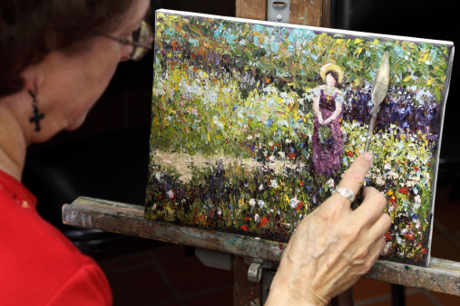 Woman artist painting on an impressionist style painting of a woman in a field of flowers.