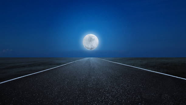 istock Asphalt road with a meadow field view with a full moon 1701578073