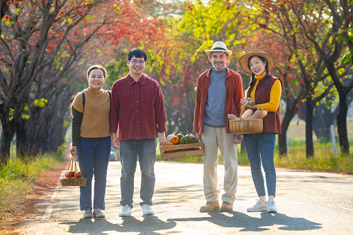Happy Asian farmer family with senior parent are carrying produce harvest with homegrown organics apple, squash and pumpkin with fall color from maple tree during autumn season for agriculture