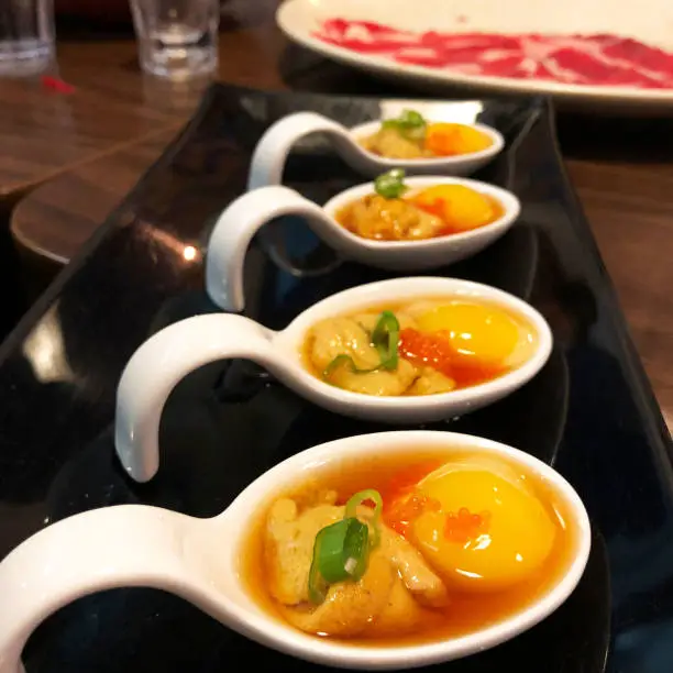 a spoonful of uni (sea urchin), raw egg yolk, and masago topped with scallions