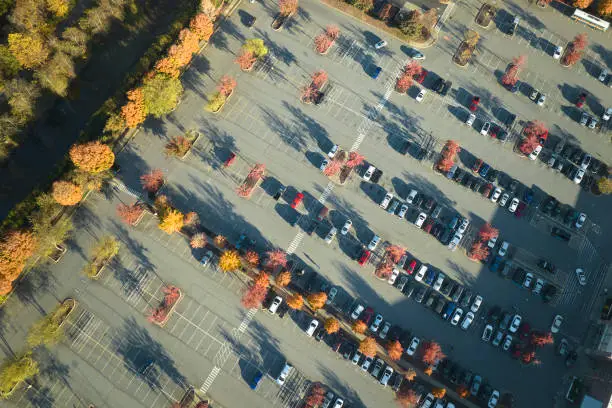 Photo of View from above of many parked cars on parking lot with lines and markings for parking places and directions. Place for vehicles in front of a strip mall center