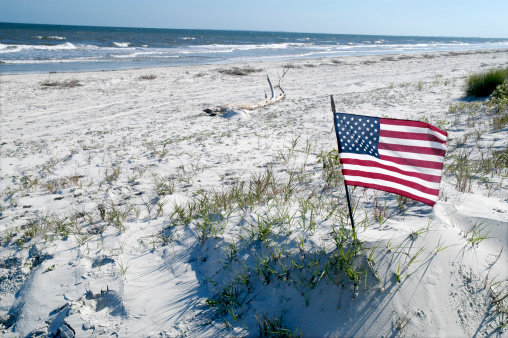 An American Flag blows in the wind on an isolated beach in South Carolina. Space for copy on left-hand side of photo.