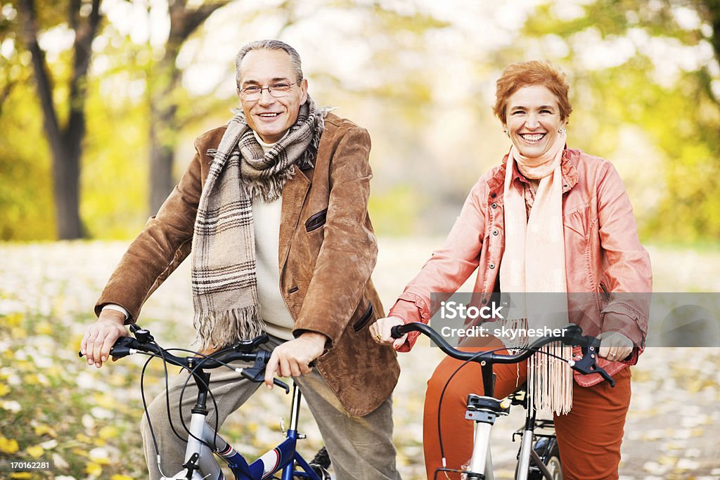 Adulto in età matura coppia biciclette equitazione nel parco. - Foto stock royalty-free di Abbigliamento casual