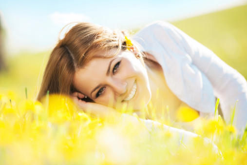 Cheerful young woman lying in the nature surrounded by  dandelions.