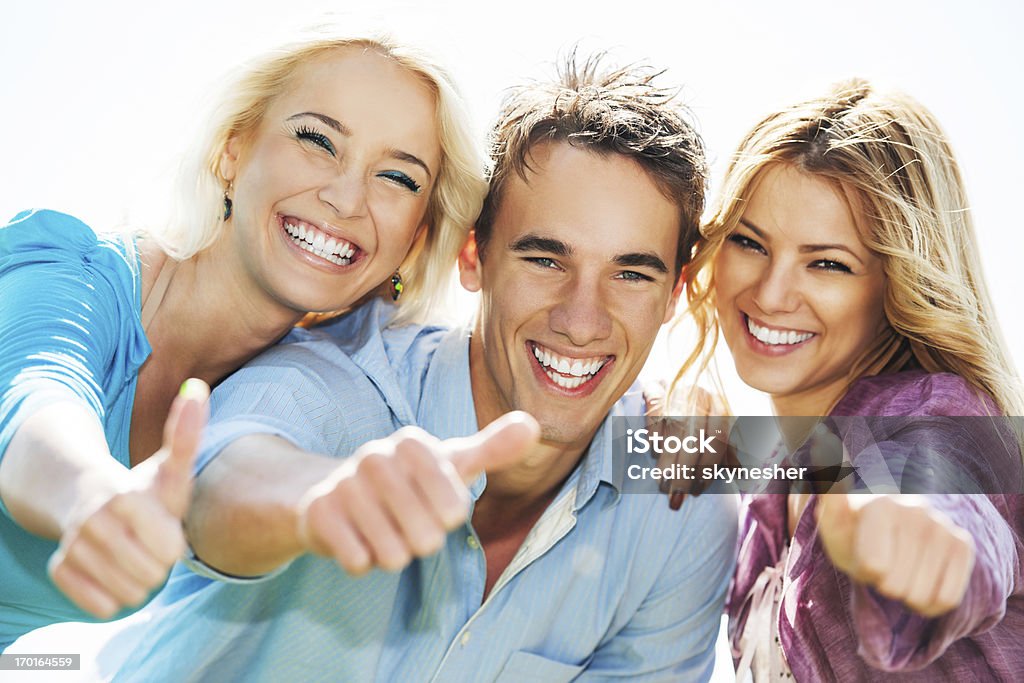 Group of friends showing thumbs up. Three cheerful friends showing ok sign and looking at camera.    Adolescence Stock Photo