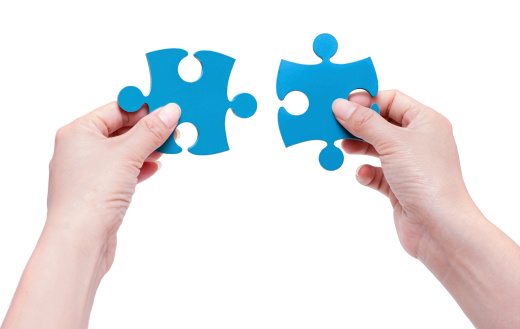 Silhouette of two hands holding and putting a piece of wooden jigsaw puzzle together