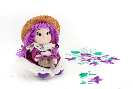 cute hand made doll in purple colours sitting on hand made tablecloth with beautiful violet embroidery