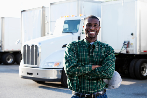 African American truck driver (20s) standing in front of semi-truck.