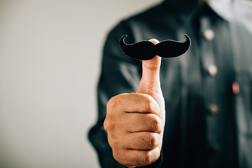 A man's thumb holds a mustache, signifying support for those affected by Prostate Cancer a powerful image for men's healthcare and World Cancer Day.